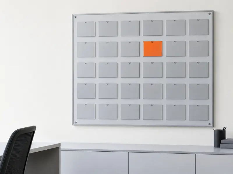 A wall-mounted job board of grey cards in a grid, with a single orange card.